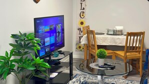 A living room with a flat-screen TV displaying a Roku interface, a glass coffee table with a potted plant, wooden chairs, and a 'WELCOME' banner. - Global Family Canada (Calgary)