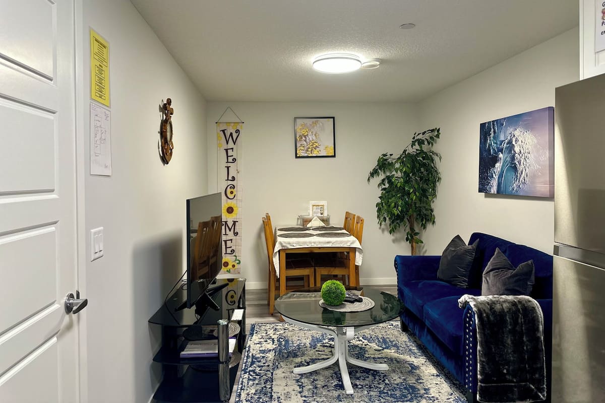 A living room with a blue sofa, a coffee table, a dining table with chairs, a TV, and a plant.