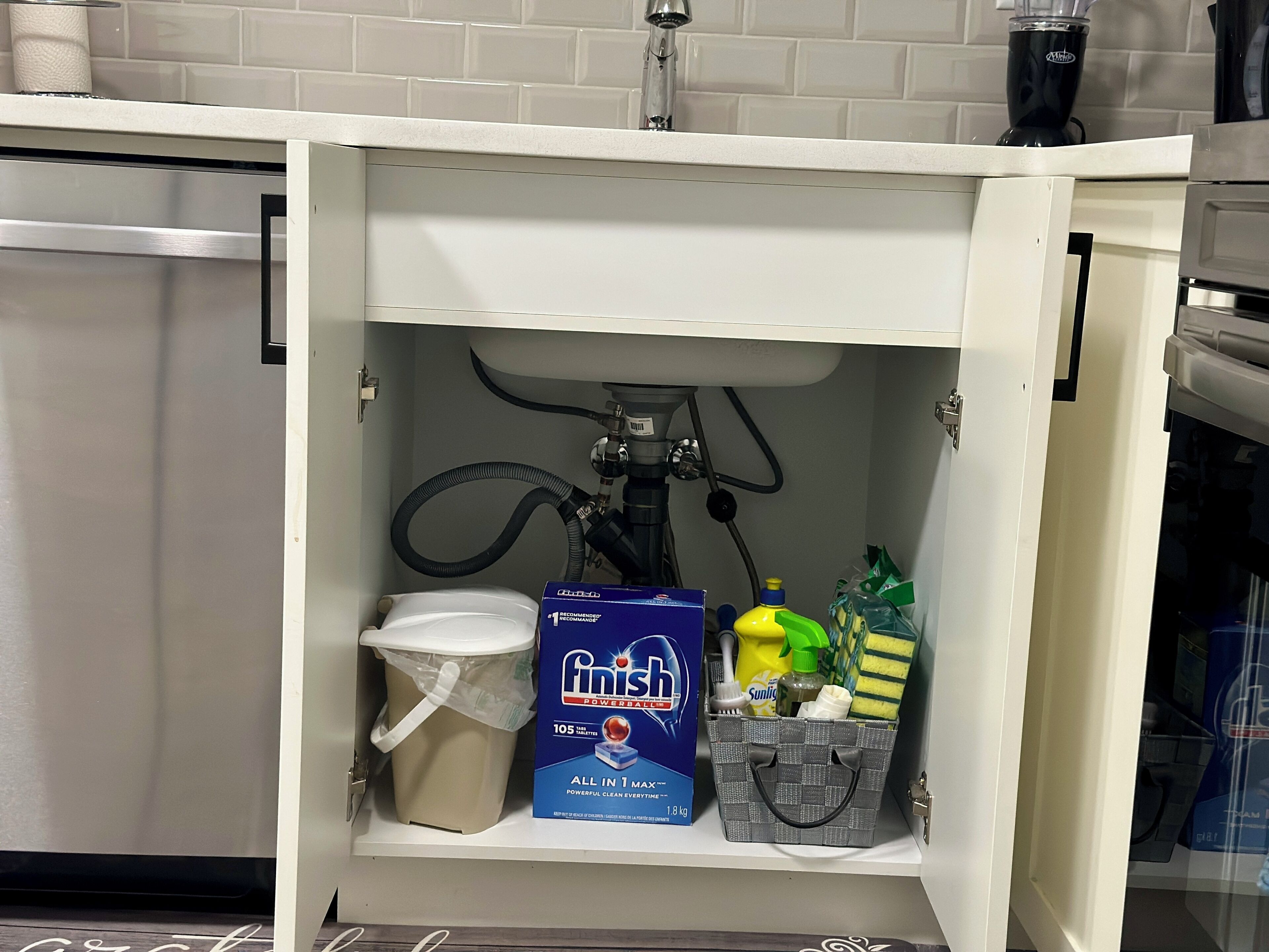 A kitchen cabinet with a built-in dishwasher, a sink, and a coffee maker.