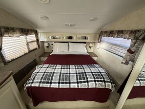 A compact bedroom with a single bed, bedside tables, a mirror, and curtains.