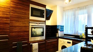 A modern kitchen with wooden cabinetry, a microwave, oven, and a washing machine. - Stunning 1-Bed Apartment in Bishop Auckland (Bishop Auckland)