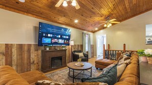 Een gezellige woonkamer met een grote flatscreen televisie, houten plafond en een open haard.