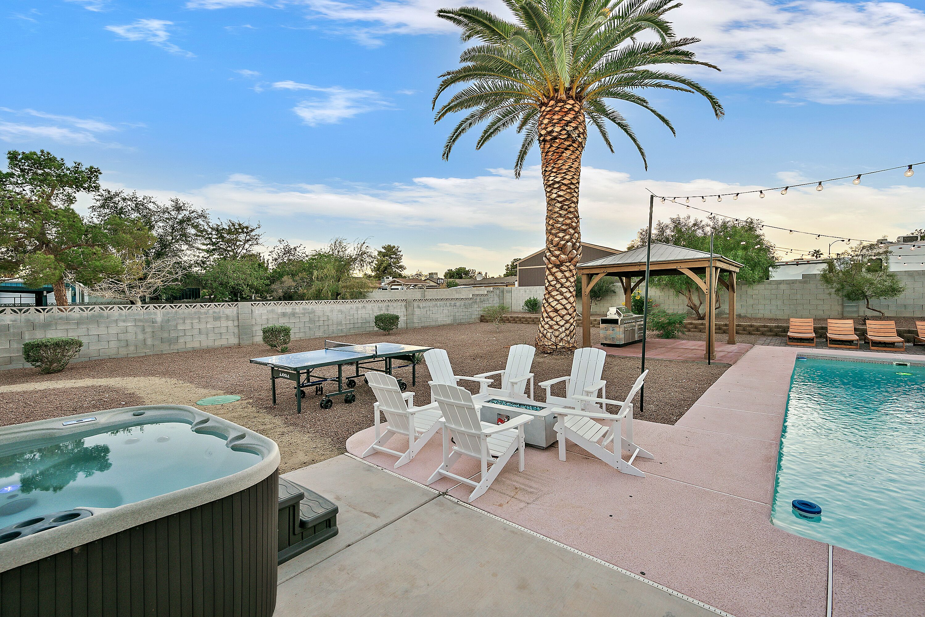 A backyard with a hot tub, outdoor seating, a pool, and a palm tree.