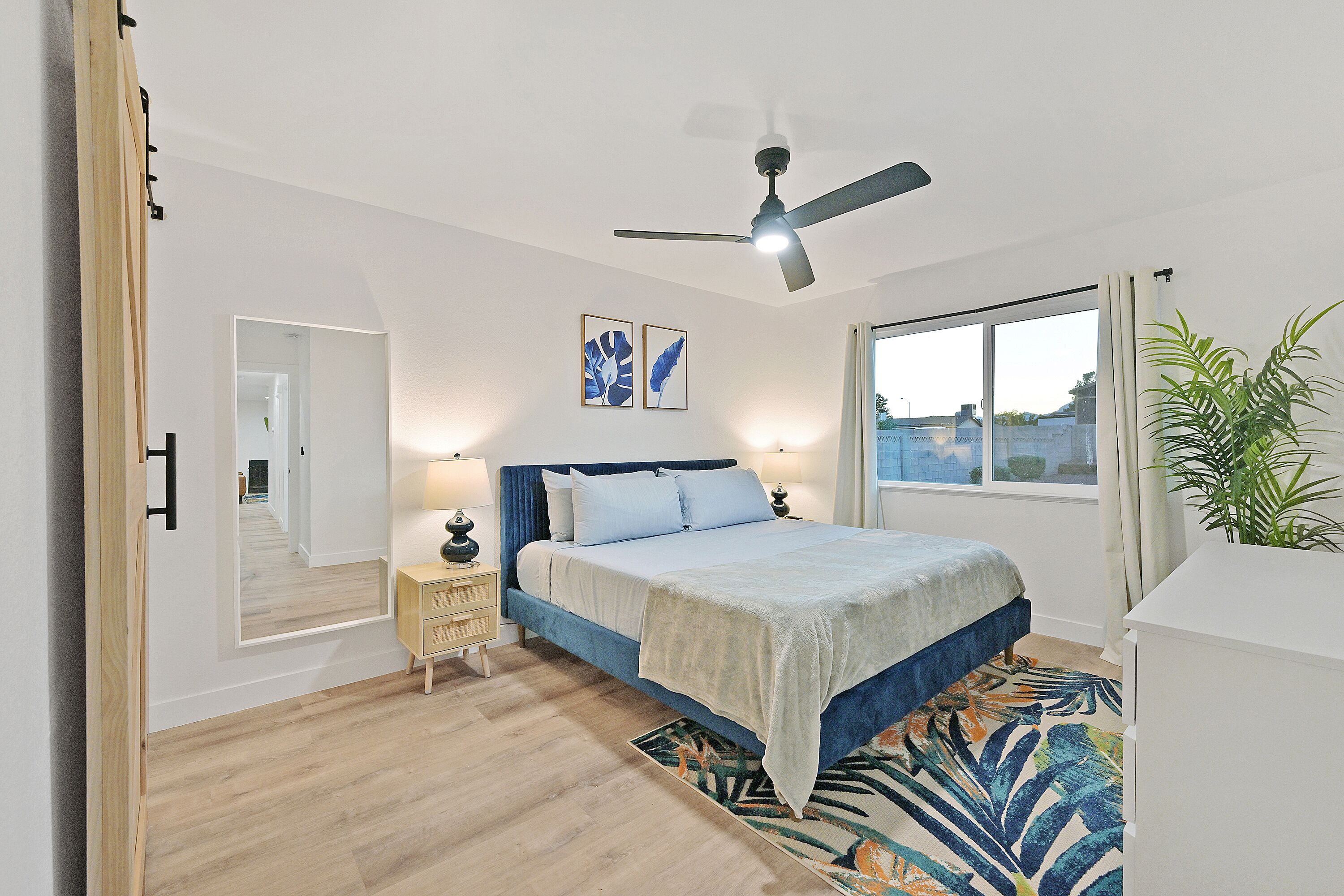 A bedroom with a bed, bedside tables, a ceiling fan, a window, and a view of the outside.