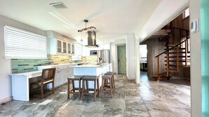 Una cocina amplia con una isla grande, taburetes de bar y una escalera de madera que sube a otro nivel.