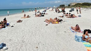 Una playa concurrida donde personas toman el sol y nadan.