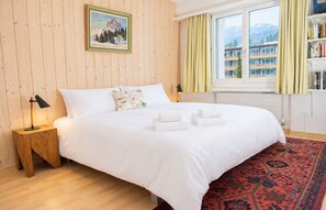 A hotel room with a bed, a nightstand, a lamp, a painting, a window with curtains, and a bookshelf. - Central base for biking and skiing (Lenzerheide/Lai)