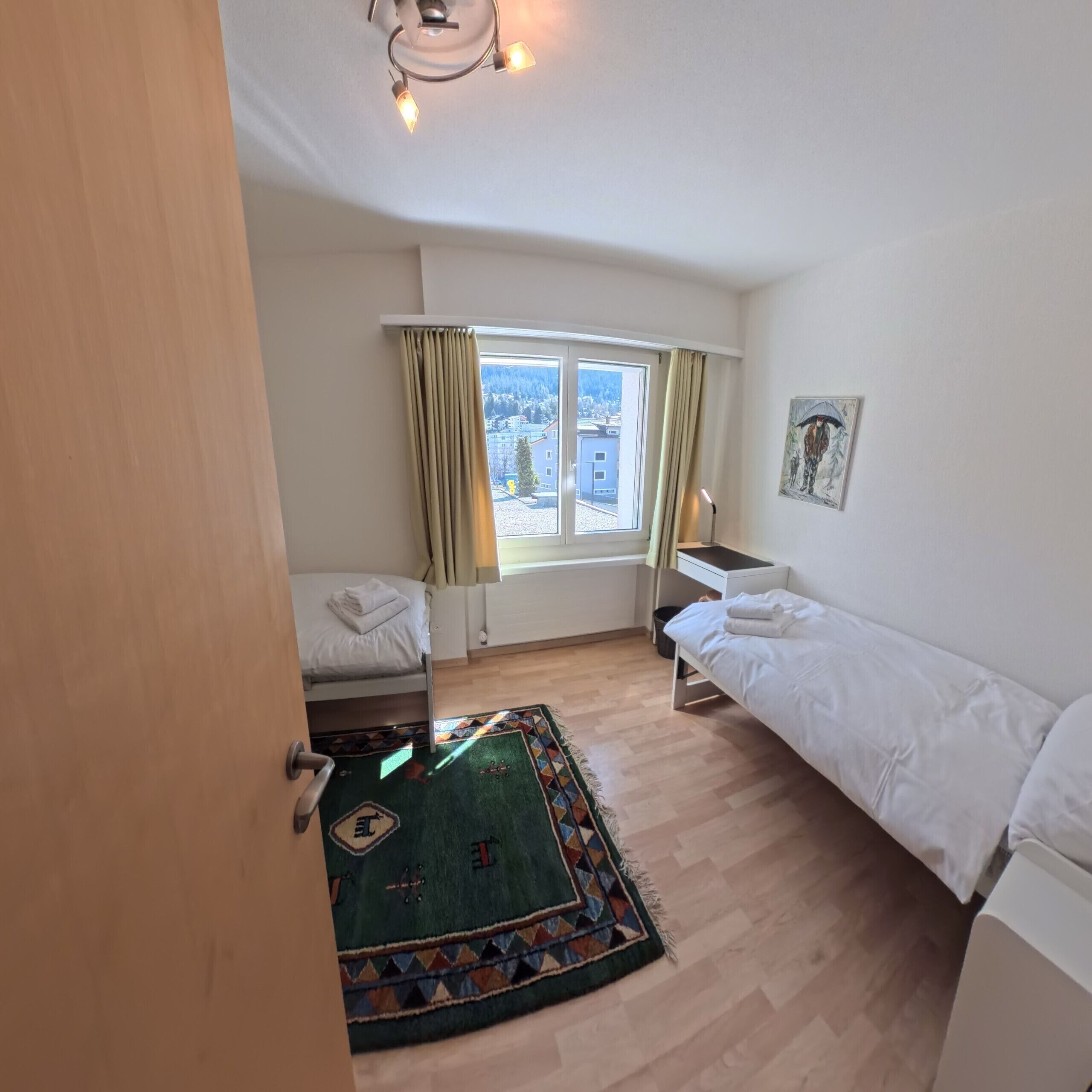Une pièce comprenant un lit, un bureau, une chaise, une fenêtre avec des rideaux, un tapis et un tableau accroché au mur.