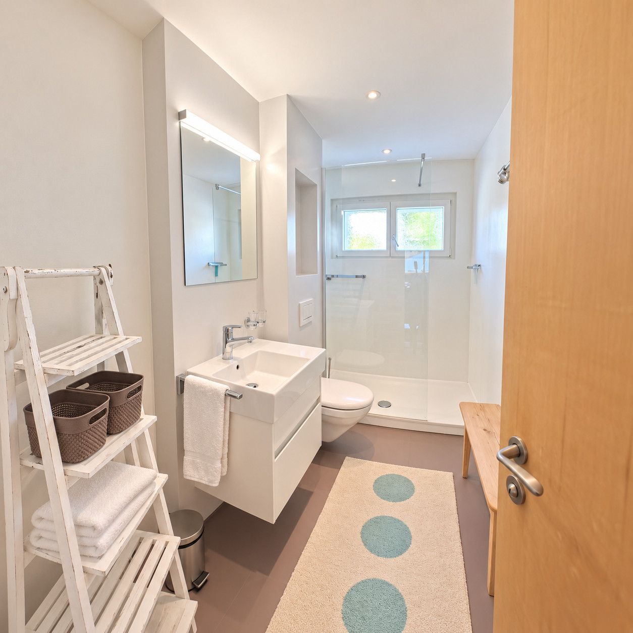 Een moderne badkamer met een wit badkamermeubel, een douchecabine met glazen wanden en een houten bankje.