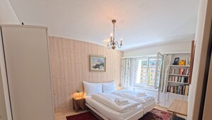 Un dormitorio con cama, mesita de noche, silla, estantería y ventana con vistas.