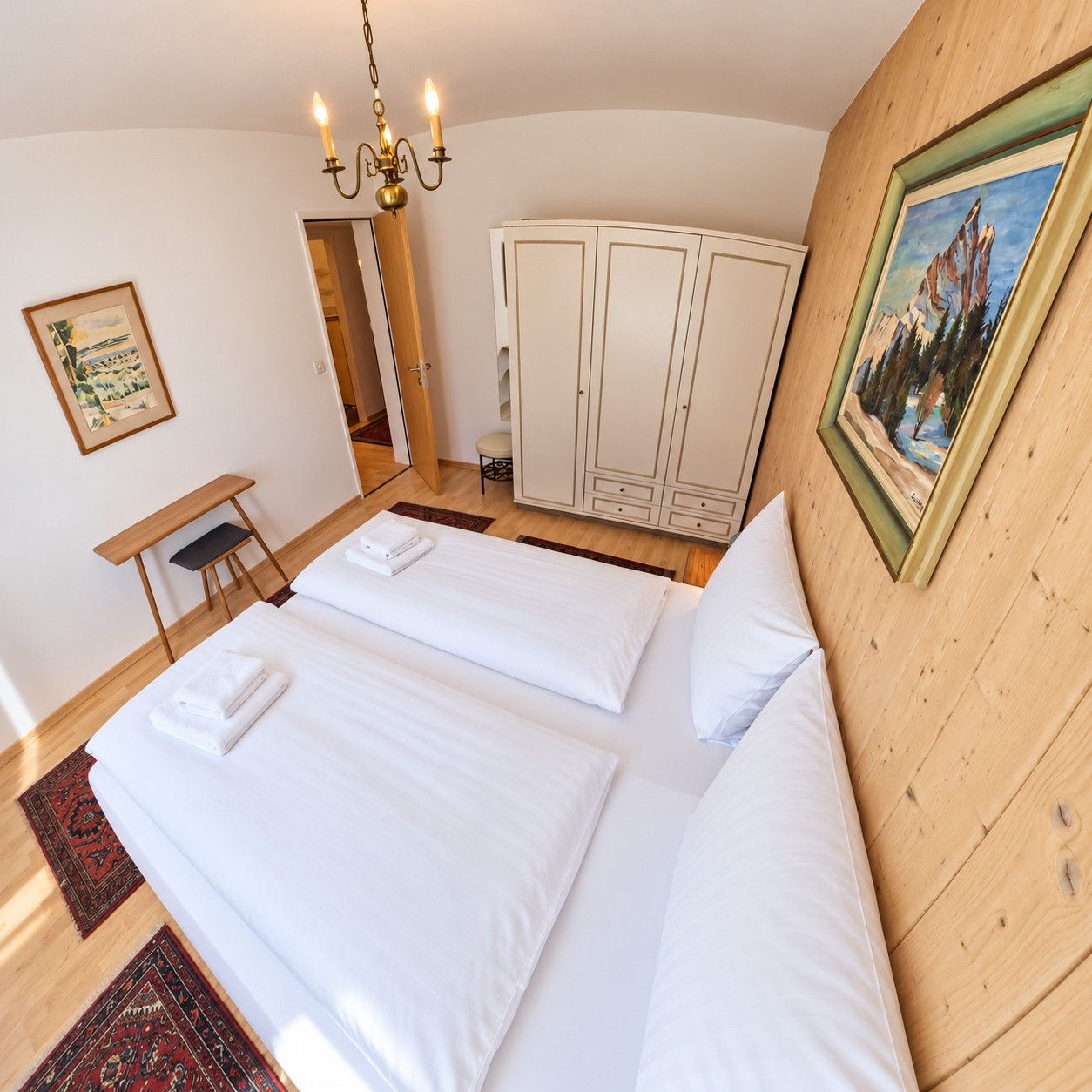 Een hotelkamer met twee bedden, een bureau, een stoel, een kledingkast en een schilderij aan de muur.