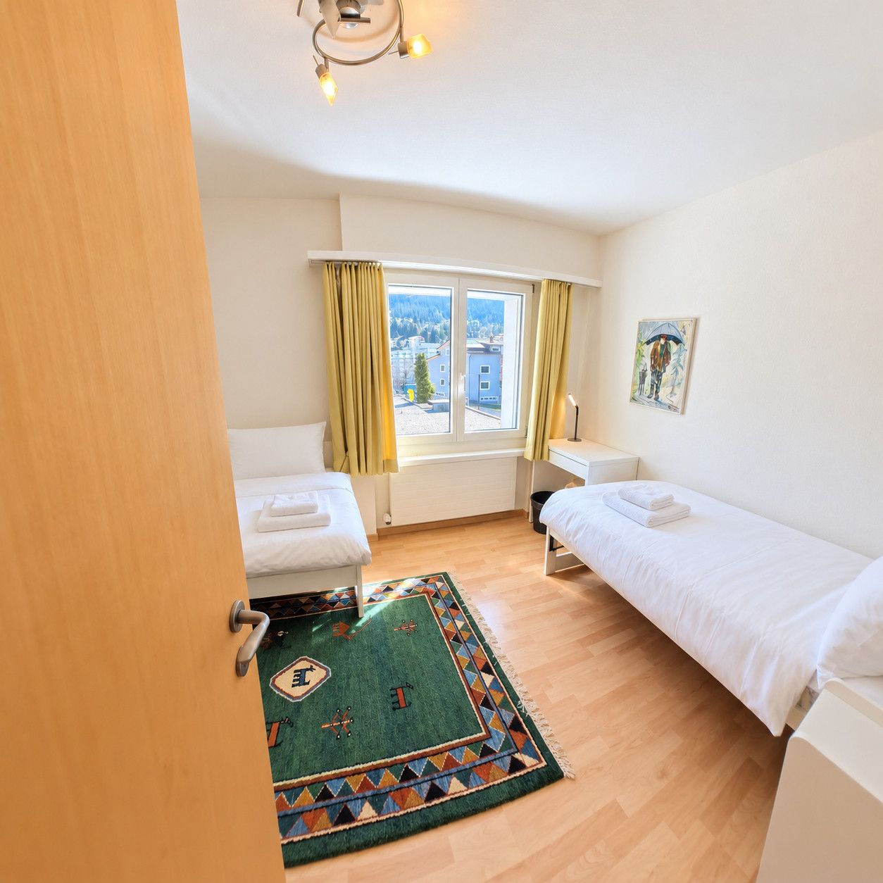 A room with two beds, a window with curtains, a painting, and a patterned rug.