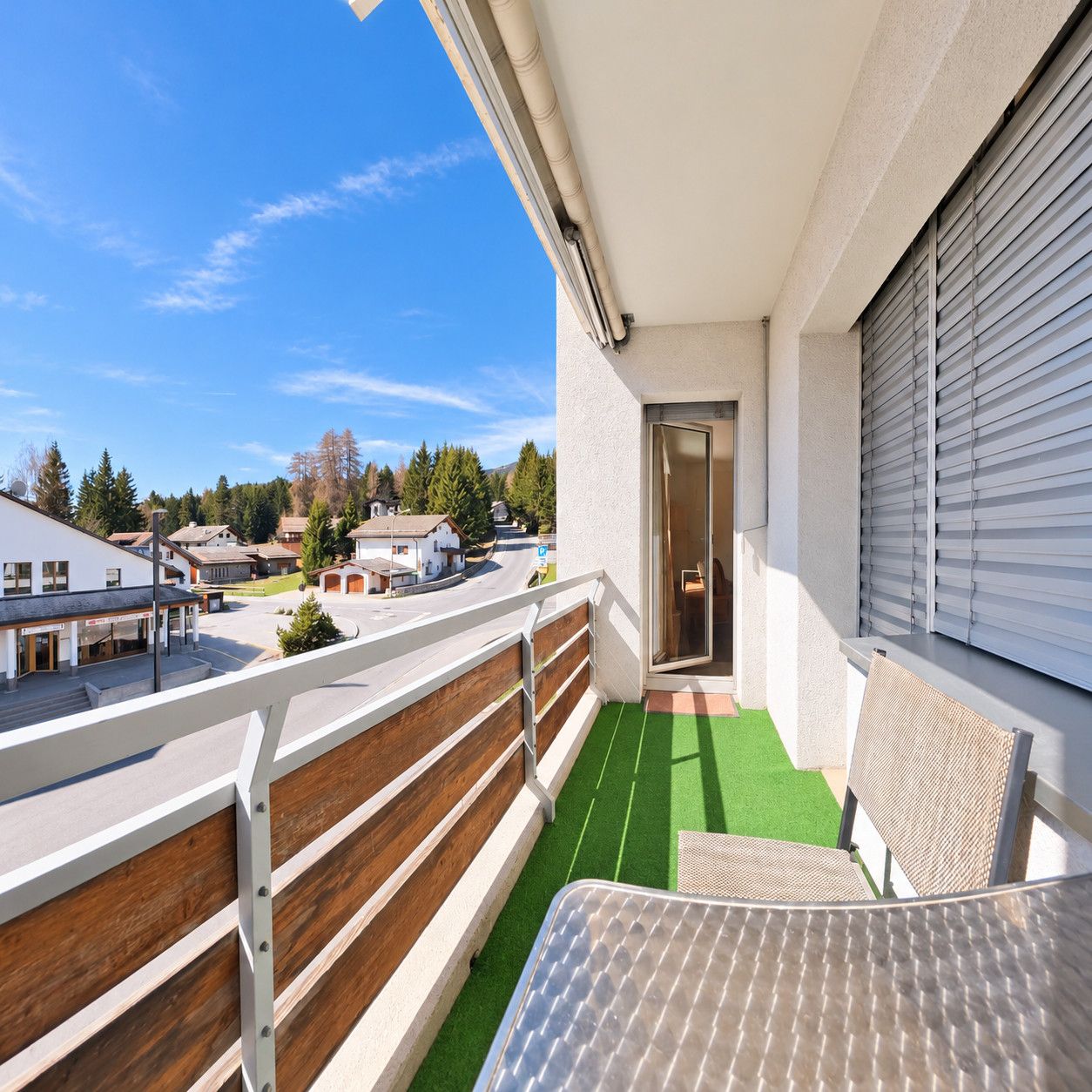 Un balcon donnant sur un quartier résidentiel, une porte menant à un espace intérieur et un petit coin salon extérieur.
