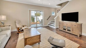 A spacious living room with a large flat-screen TV, a wooden coffee table, a leather armchair, and a sofa.