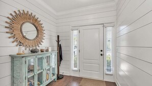 A hallway with a white door, a wooden-framed mirror, and a teal cabinet with glass doors.