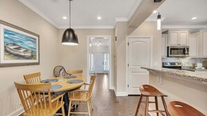A dining area with a round table and chairs, a kitchen with white cabinets and stainless steel appliances, and a hallway leading to a door.
