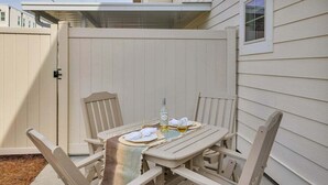 A patio with a table set for two, surrounded by wooden chairs, and a beige fence enclosing the space.