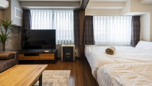 Une chambre d’hôtel moderne équipée d’une télévision à écran plat, d’une table basse en bois, d’un lit avec du linge de maison blanc et d’une plante en pot.