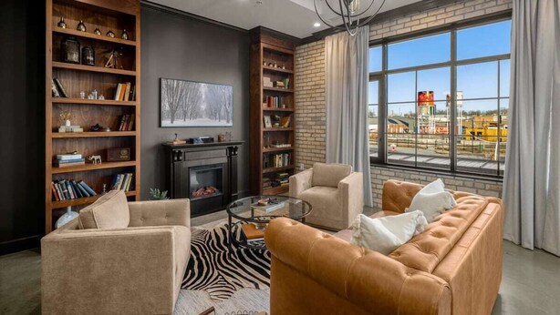A modern living room with a fireplace, leather sofas, and large windows offering a view of the city. - Perfect for Couples-Walk Everywhere-Luxe Apt (Rogers)