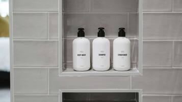 Tres botellas blancas de jabón corporal, champú y acondicionador sobre una pared de baldosas.
