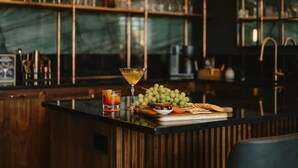 A bar area with a wooden counter, a martini glass, a glass of whiskey, and a bowl of grapes. - Perfect for Couples-Walk Everywhere-Luxe Apt (Rogers)