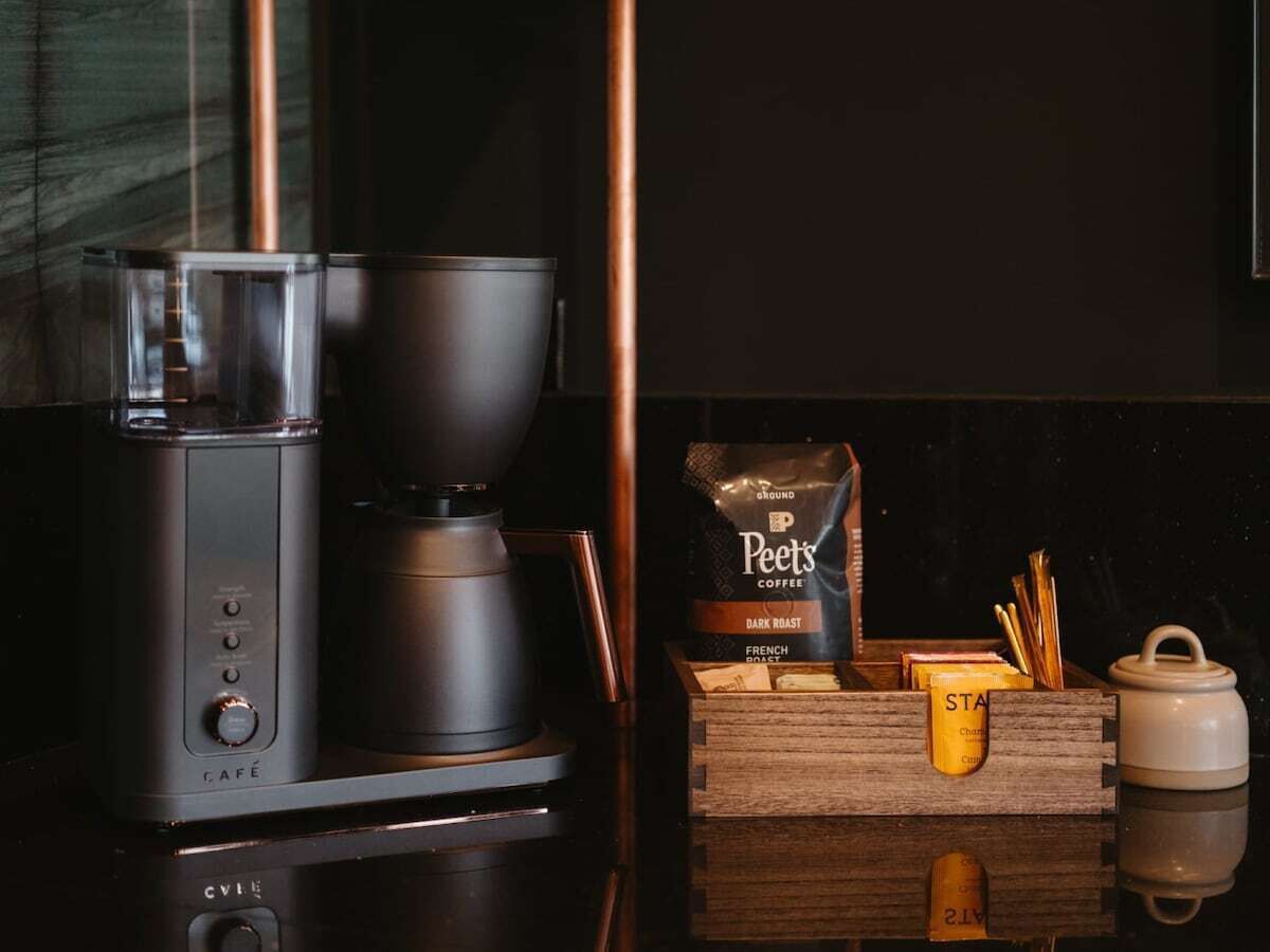 A coffee maker, Peet's Coffee bag, and a wooden box with a yellow container on a kitchen counter.