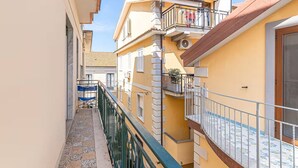 Une ruelle étroite entre deux immeubles dotés de balcons, un petit espace extérieur aménagé avec des sièges et un sol carrelé.