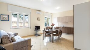 Un appartement moderne comprenant un salon, un coin repas et une cuisine. Le salon est équipé d’une télévision, le coin repas d’une table et de chaises, et la cuisine est aménagée avec des placards et un évier.