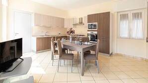 Une cuisine moderne avec un coin repas, comprenant un îlot central, un four encastré et une grande fenêtre avec des rideaux.