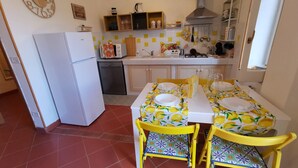 Una cocina compacta equipada con refrigerador, lavavajillas y una mesa para dos personas con sillas amarillas.