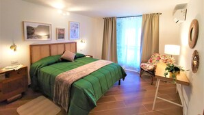 Un dormitorio con cama, escritorio con lámpara, silla, cómoda y ventana con cortinas.