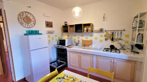 Una cocina compacta con refrigerador, horno, microondas y pileta. Hay una mesa de comedor con mantel estampado de limón y una silla amarilla. La cocina tiene un salpicadero de azulejos y una lámpara colgante.