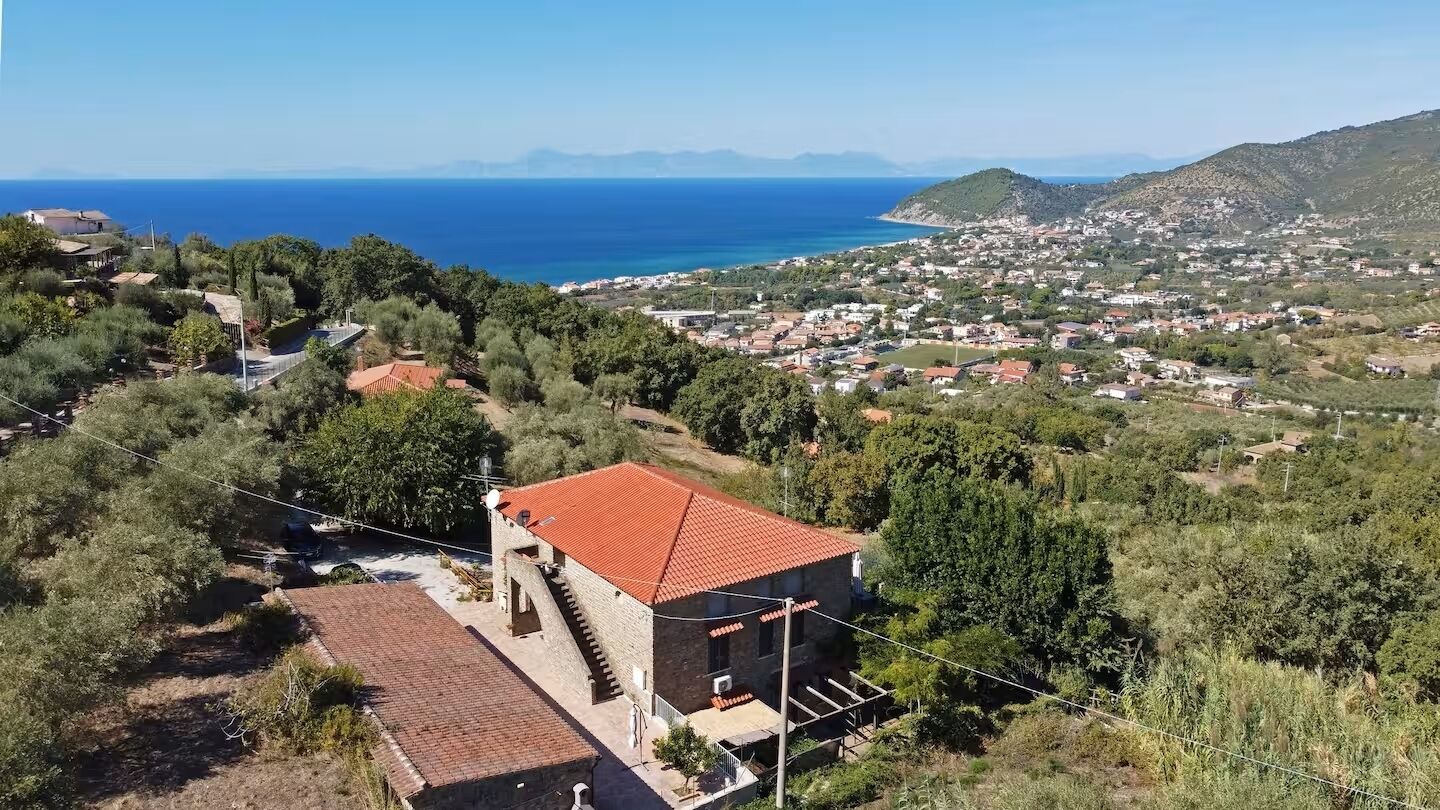 A coastal village with a prominent red-roofed building surrounded by greenery and a view of the sea.