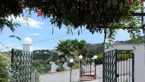 A gated entrance with a decorative pavement design, a white wall, and a view of a hilly landscape.