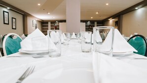 Una mesa de comedor dispuesta con manteles blancos, cristalería y cubiertos, y sillas color turquesa.
