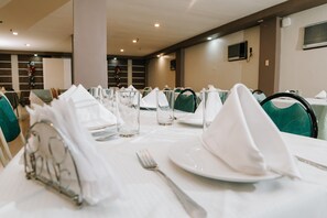 Un comedor con mesas dispuestas para una comida, incluyendo platos, cubiertos y servilletas.
