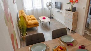 Een eetgedeelte met een tafel gedekt voor twee personen, een bank, een ventilator en een televisie op de achtergrond.