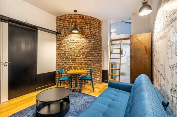 Una habitación con pared de ladrillo, un sofá azul, una mesa redonda y dos sillas.