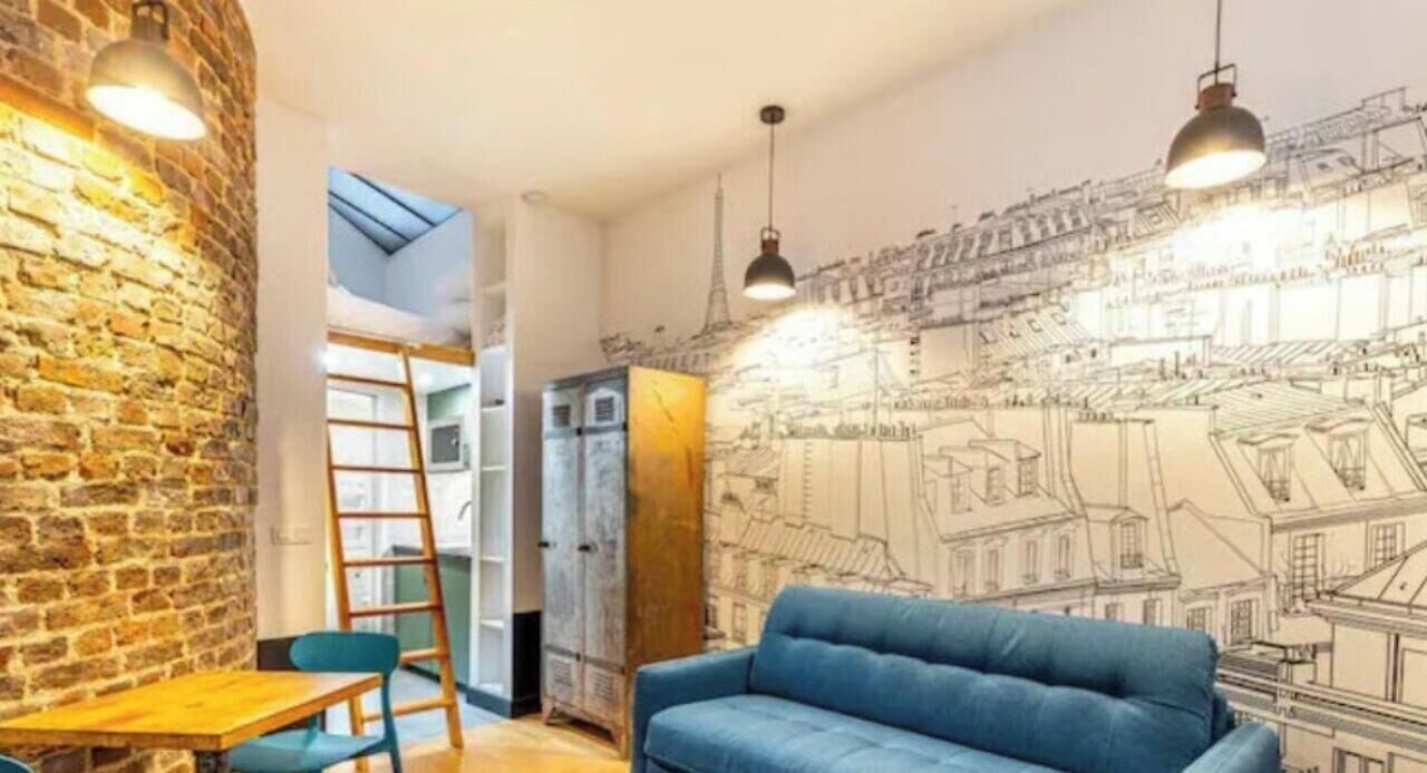 Ein Zimmer mit einer Ziegelwand, einem blauen Sofa, einem Holztisch und einer Leiter.