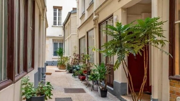 A narrow alleyway with potted plants and a red door at the end.