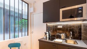 A compact kitchen with a microwave, toaster, and kettle on the counter, a window with blinds, and a door leading to another room.