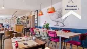 Un restaurante con varias mesas y sillas, un mural de un ave en la pared, y un letrero que indica que es recomendado.
