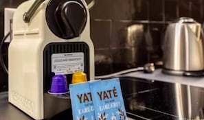 A coffee machine with a label and two colored cups, a kettle, and a bag of Earl Grey tea.