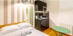 A compact hotel room with a bed, a small kitchenette, and a green table.
