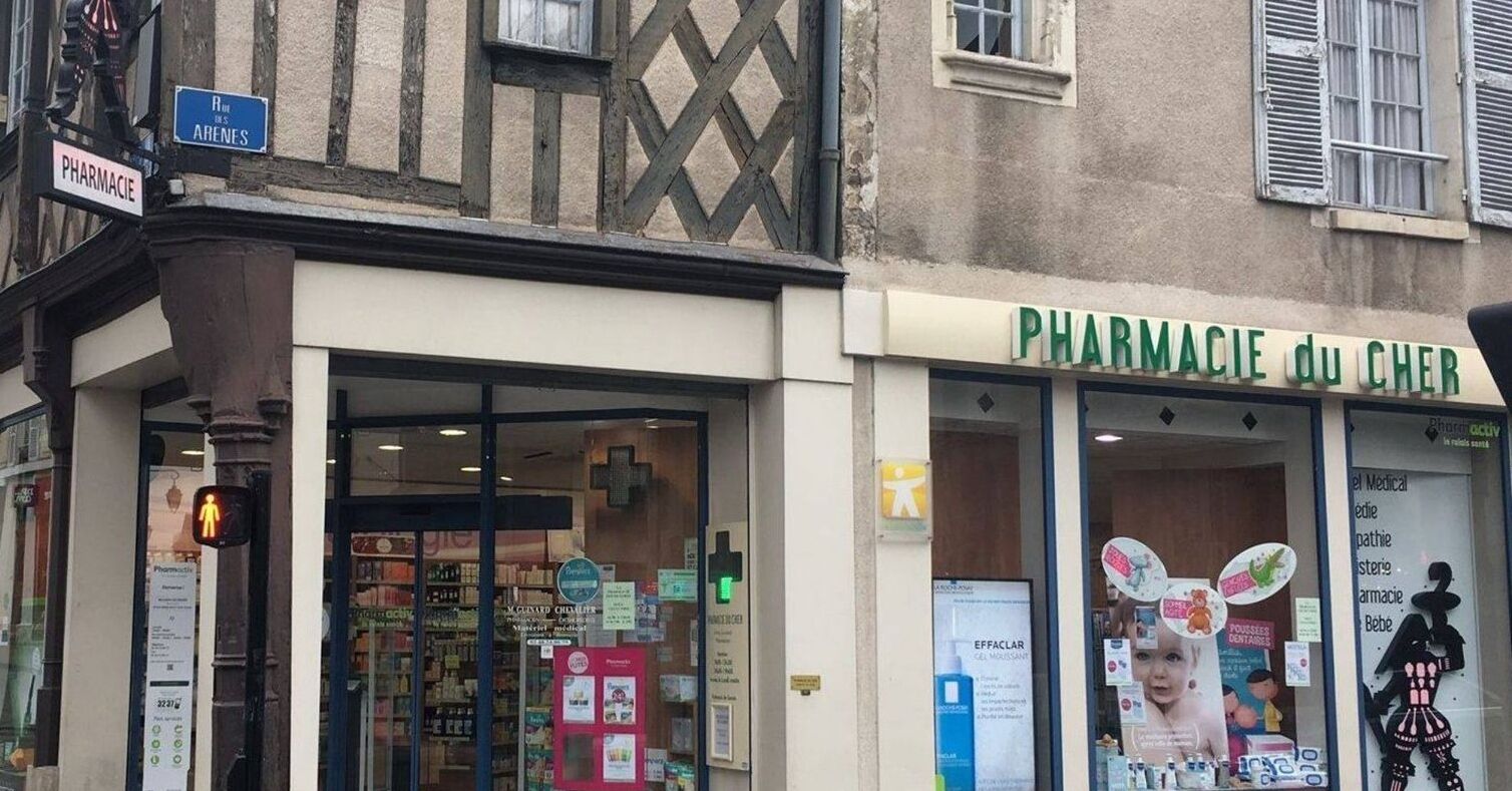 A pharmacy with a sign reading "PHARMACIE du CHER" and a pedestrian crossing signal.