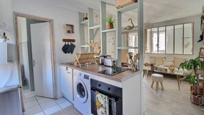 Ein kompakter Wohnraum mit Küchenzeile, Waschmaschine und Essbereich mit Sofa und Tisch.