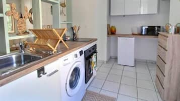 Une cuisine compacte équipée d’un lave-linge intégré, d’un petit réfrigérateur et d’un four à micro-ondes.
