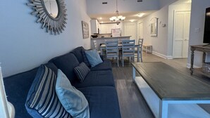 A modern living room with a dark blue sofa, a wooden coffee table, and a dining area with a white table and chairs.