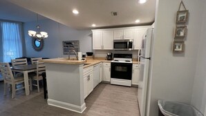 A modern kitchen with white cabinets, a central island, a microwave, an oven, and a refrigerator.