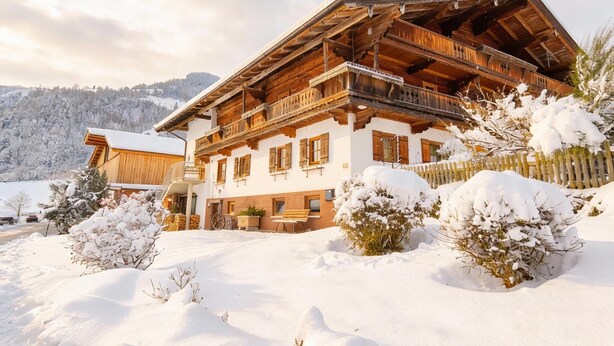 A traditional wooden chalet with a sloped roof, wooden balconies, and a snow-covered landscape. - Two modern holiday flats on the farm, ski-out (Itter)